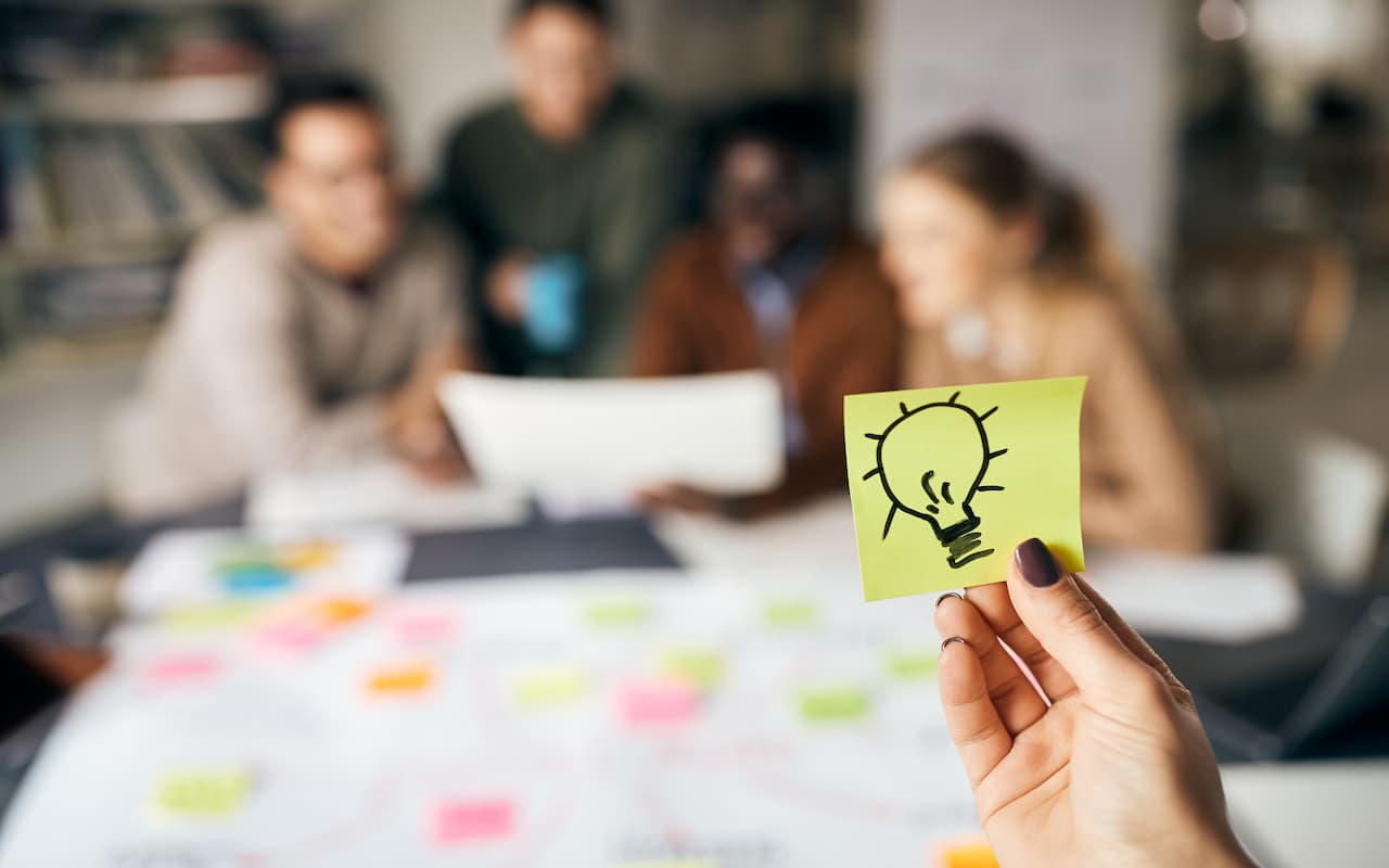 Drawing of a lightbulb on a note while marketers are brainstorming